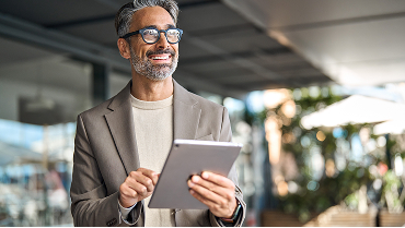 A business owner holds a tablet computer and smiles broadly, knowing his employees have affordable health care.