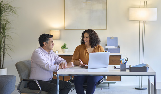 A man and woman in an office talking behind a desk.