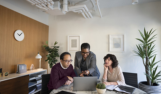 Three professionals sitting a table looking at a laptop screen