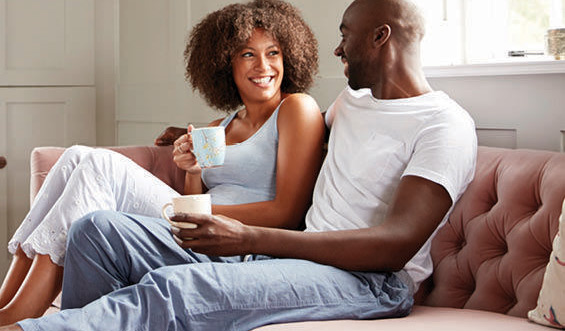 A young, smiling couple drinks coffee on a couch.