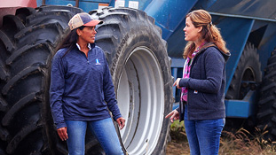 Two farmers having a conversation next to heavy farm equipment