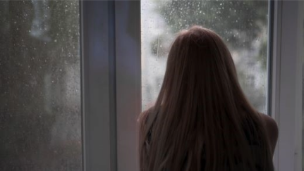  A woman looks out a house window during hurricane weather