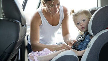woman fastening child in car seat