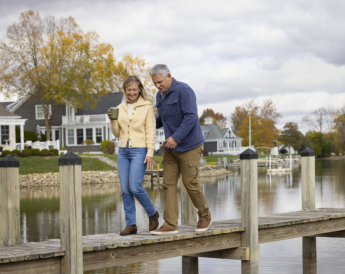 A retired married couple walk along a pier surrounding a small lake.