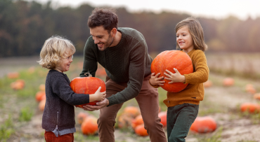 un niño y una niña en un huerto de calabazas con un hombre