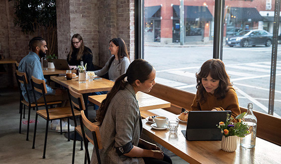 Two women talk over a computer at a coffee shop.