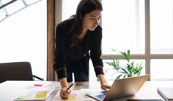 Woman standing over a desk looking at a laptop