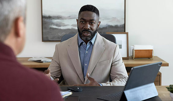 A man sits at a desk talking to someone across from him.