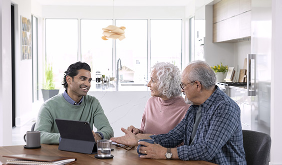 A smiling man shows an elderly couple something on a tablet.