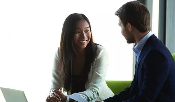 a man and a woman smile at each other next to laptop