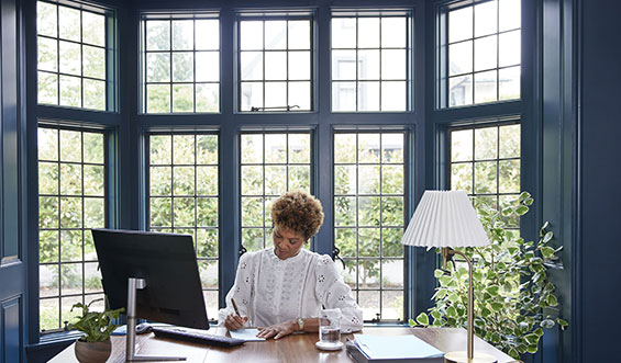 Woman sitting at a desk with a computer and writing something.