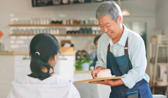 Older man serving a slice of cake to a woman in a bakery