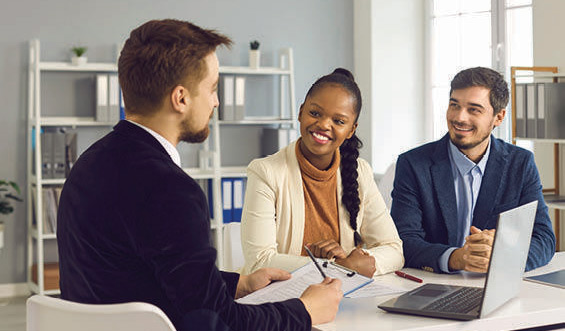 Three business people smile in a meeting at a conference table.