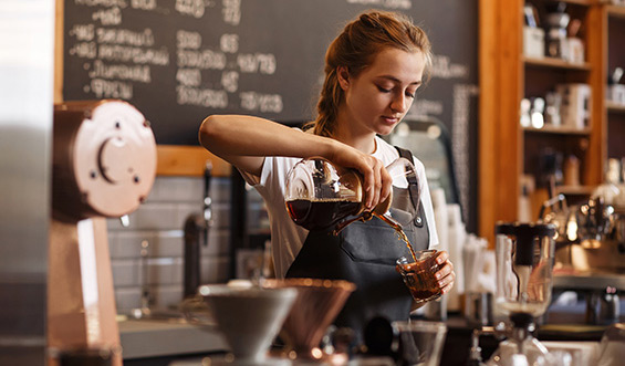 A barista pouring a drink in a glass.