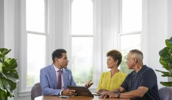 Two men and a woman talk at table with a tablet