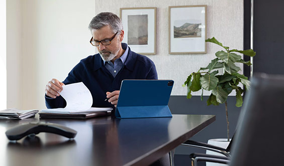 A man sits at a desk with a notepad and a tablet.