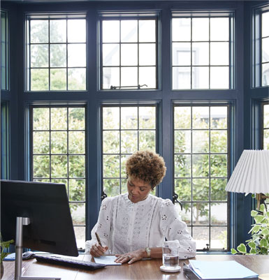 Woman sitting at a desk with a computer and writing something.