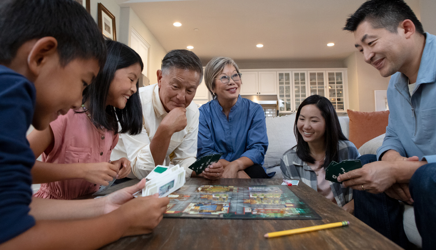 A retired couple laughs while playing a board game with their daughter, son-in-law and grandchildren.