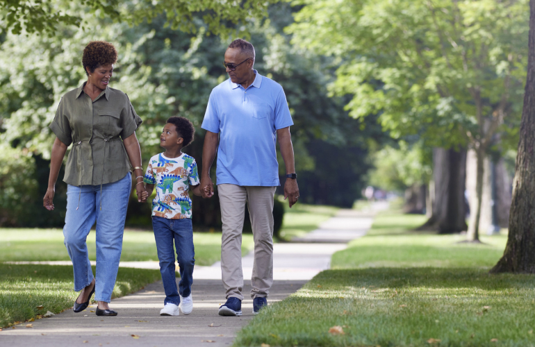 A retired couple takes a walk through their tree-lined neighborhood with their grandson.