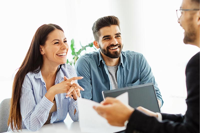 A financial professional discusses the benefits of guaranteed retirement income with a millennial couple in a bright, professional meeting room.