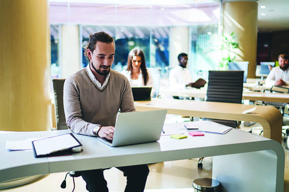 Man in his 30s or 40s wearing business clothes, sits at computer by himself in the office, typing.