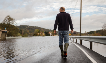 Man walking in a flooded road wearing rain boots.