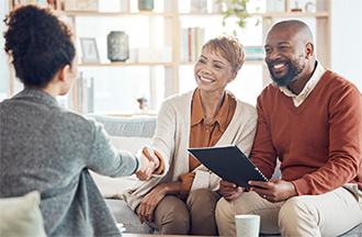 A photo of a financial professional sitting across from a couple and shaking hands with a woman.